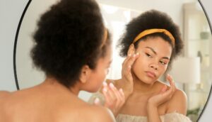 African american black woman looking touching face in the mirror examining skin condition and acne