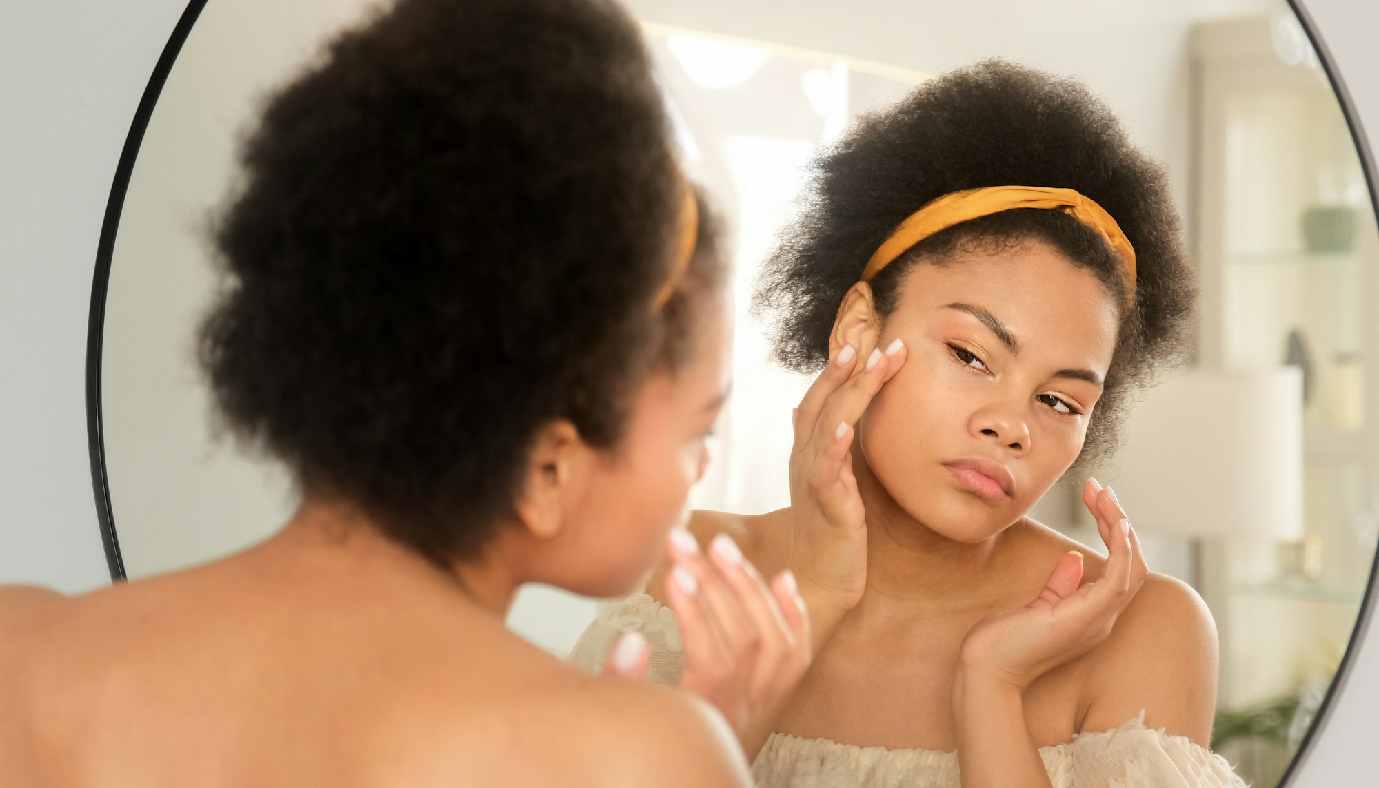 African american black woman looking touching face in the mirror examining skin condition and acne