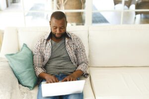 African american man using laptop sitting on couch in living room