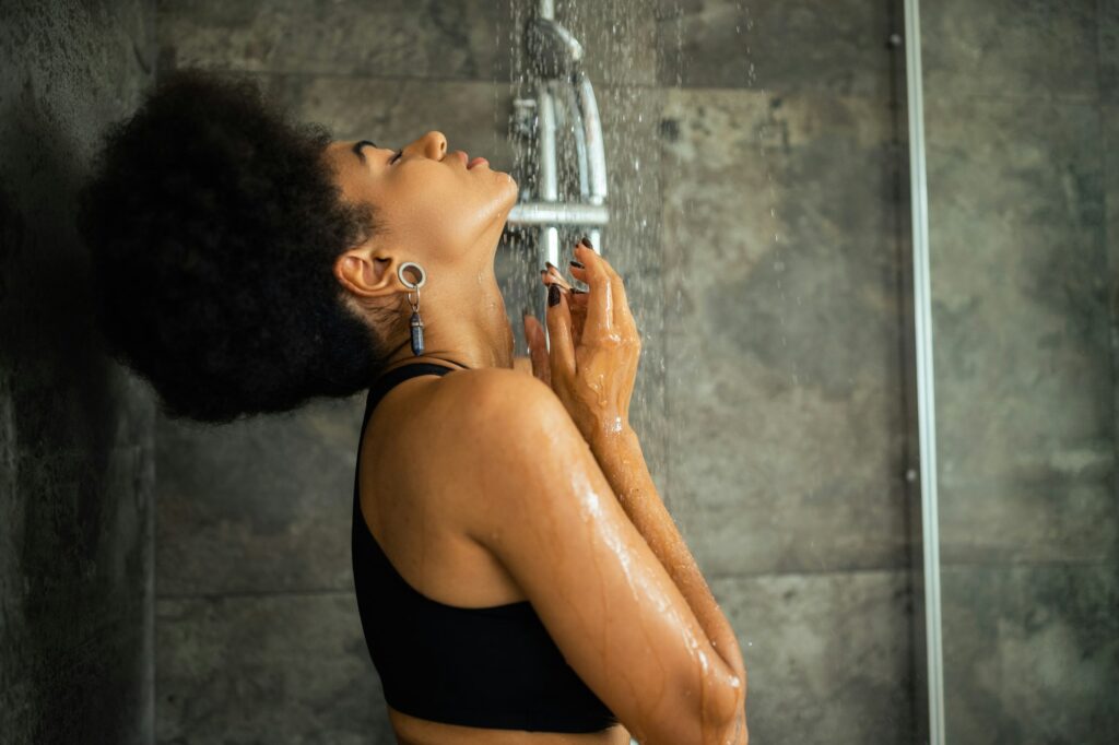 Side view of young african american woman in crop top taking shower at home