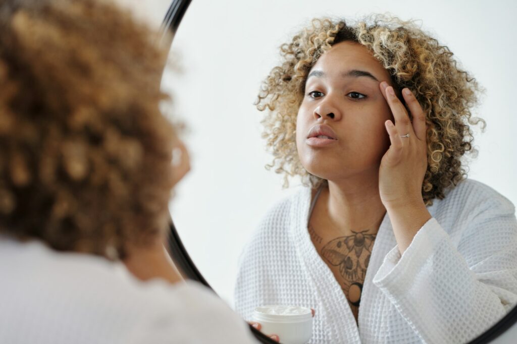 Young African American woman applying lotion on skin of eyelid