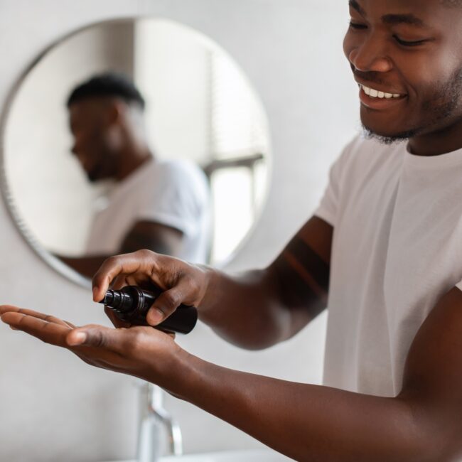 Black Man Squeezing Bottle Caring For Facial Skin In Bathroom