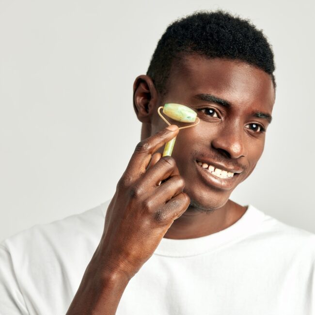 Black guy with youthful skin using jade de-puffing face roller to keep his skin soft and smooth