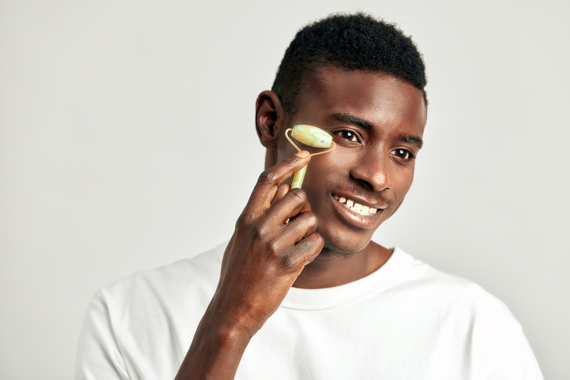 Black guy with youthful skin using jade de-puffing face roller to keep his skin soft and smooth